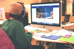 a student sits at his computer wearing headphones 